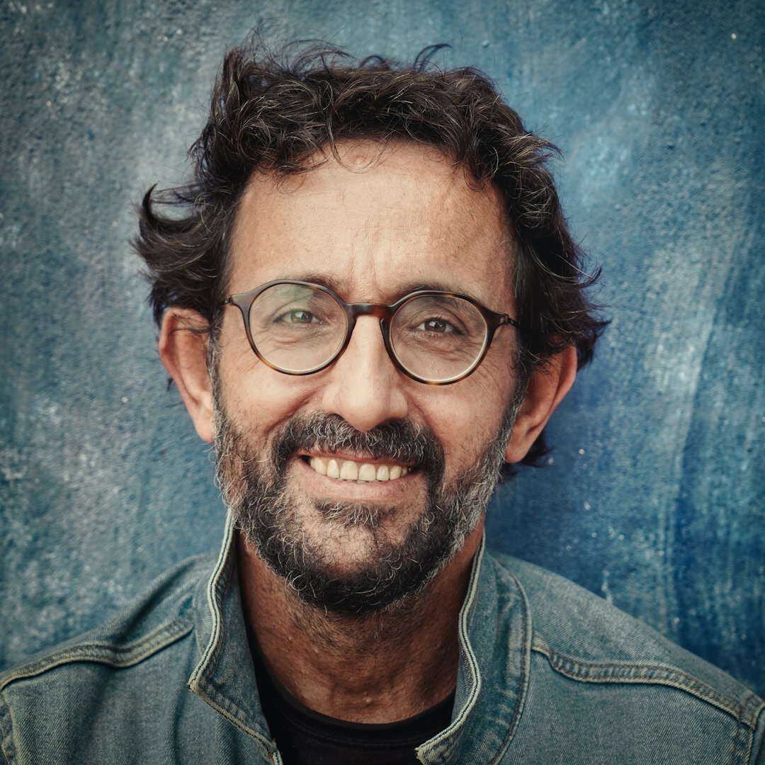 Studio portrait of a bearded man in his forties wearing glasses and a shirt